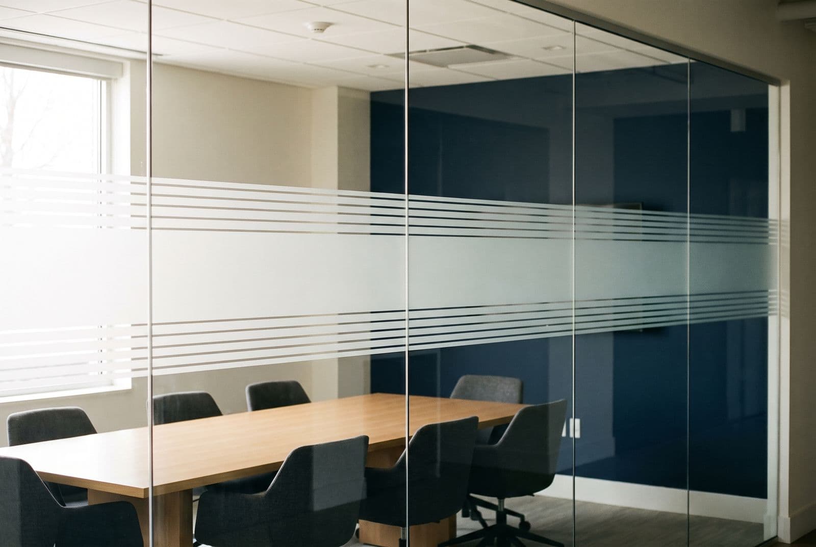 A conference room enclosed in frameless glass carrying a wide band of frosted decorative film at seated height, clear glass above and below